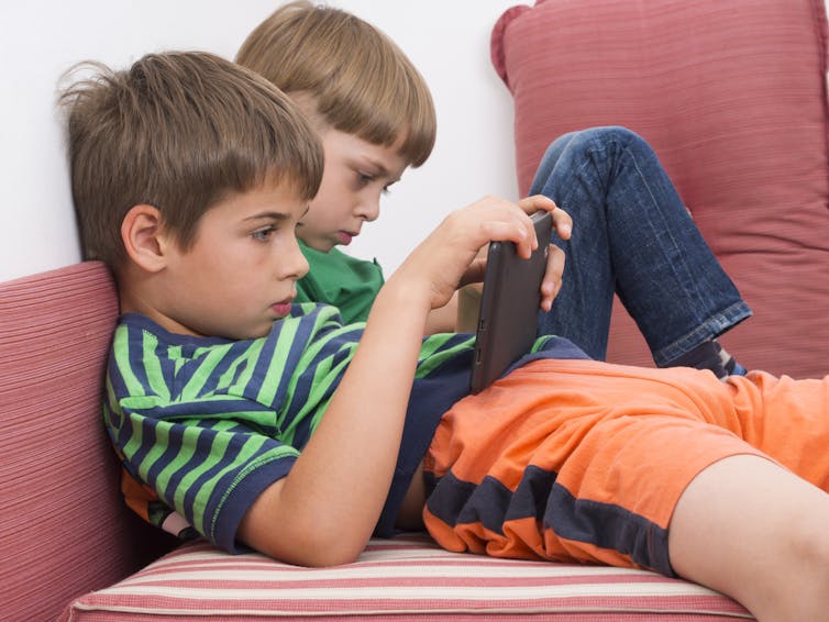 Two boys slumped on a sofa, holding tablet computers