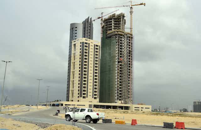 A car drives in front of modern skyscrapers under construction with large cranes alongside
