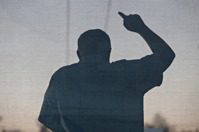 Contraluz de un hombre durante un discurso con gesto amenazador.
