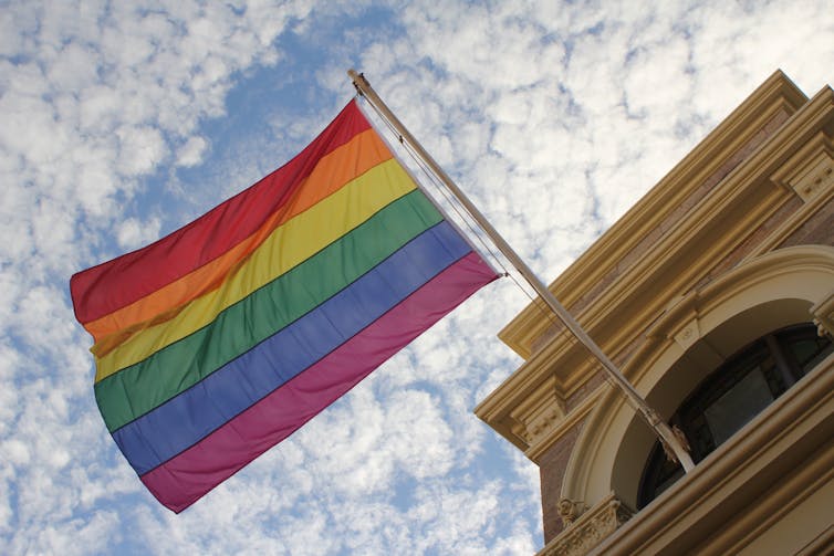 Rainbow flag flying against a blue sky.