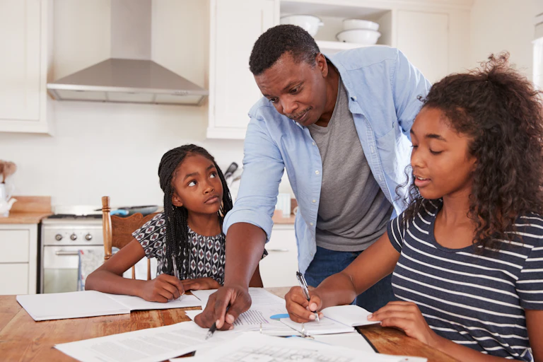 Father pointing out something to two daughters doing their schoolwork
