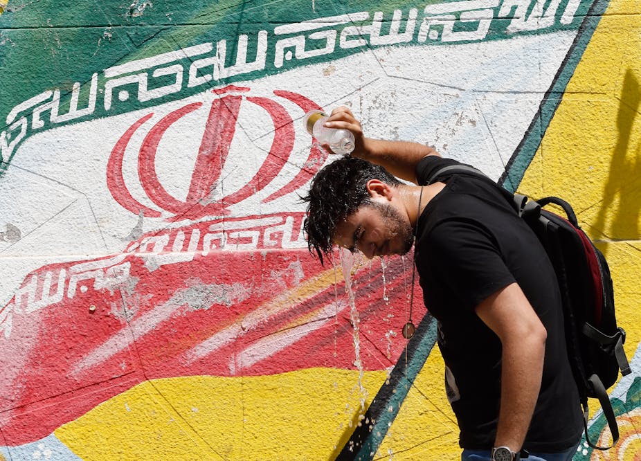 Man pouring bottle water over head in front of Iranian flag.