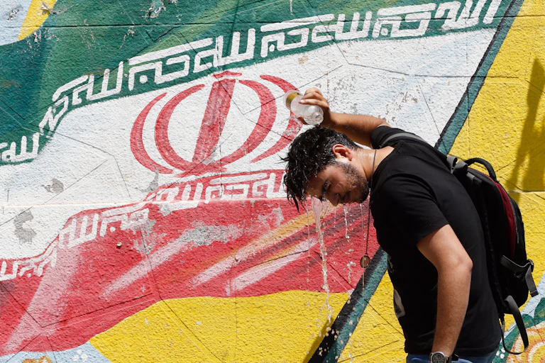 Man pouring bottle water over head in front of Iranian flag.