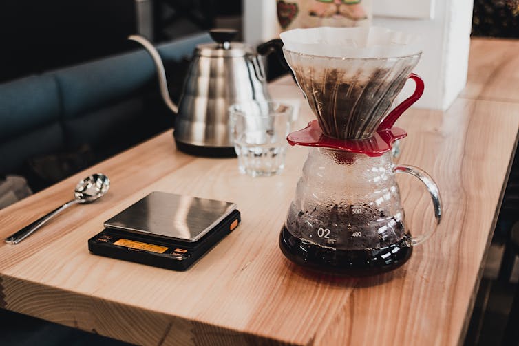 Table with V60 coffee dripper next to scales, spoon and kettle.