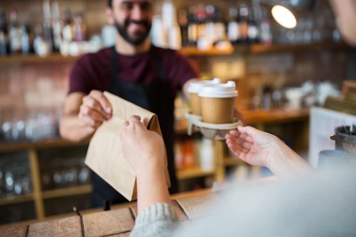 Barista hands takeaway coffee and bag to customer. 