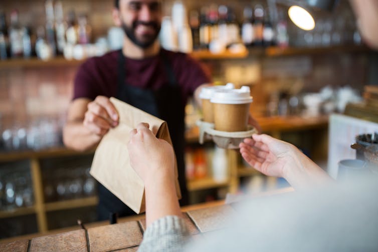 Barista hands takeaway coffee and bag to customer.