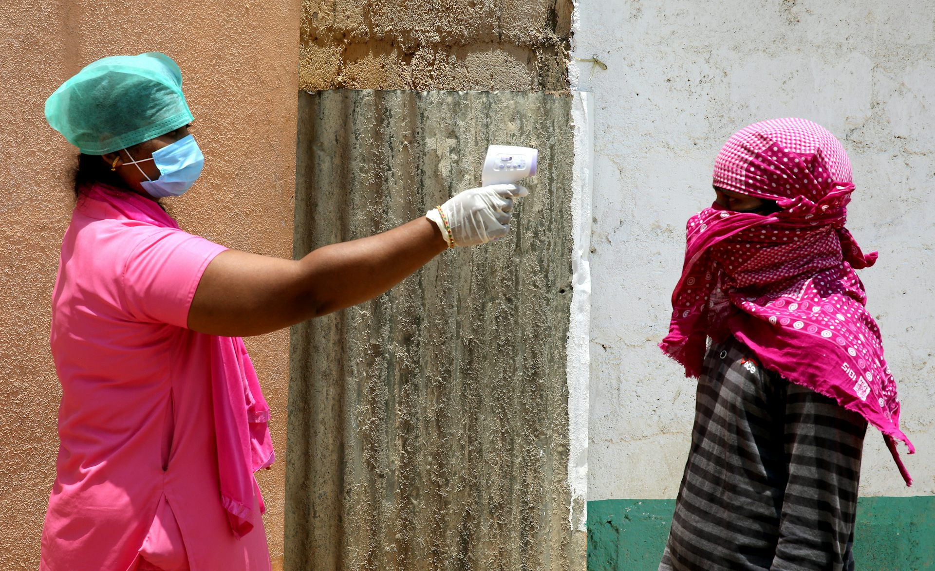 A health worker in PPE uses an electronic thermometer to check the temperature of a worker.