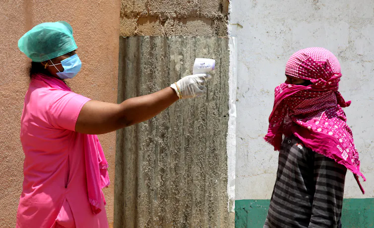 A health worker in PPE uses an electronic thermometer to check the temperature of a worker.