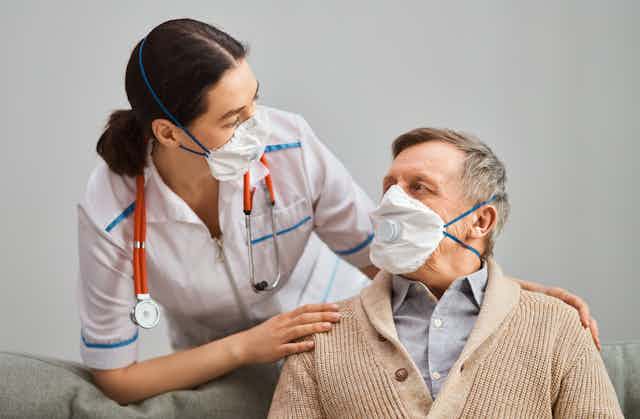 An older man, wearing a mask, interacting with a nurse