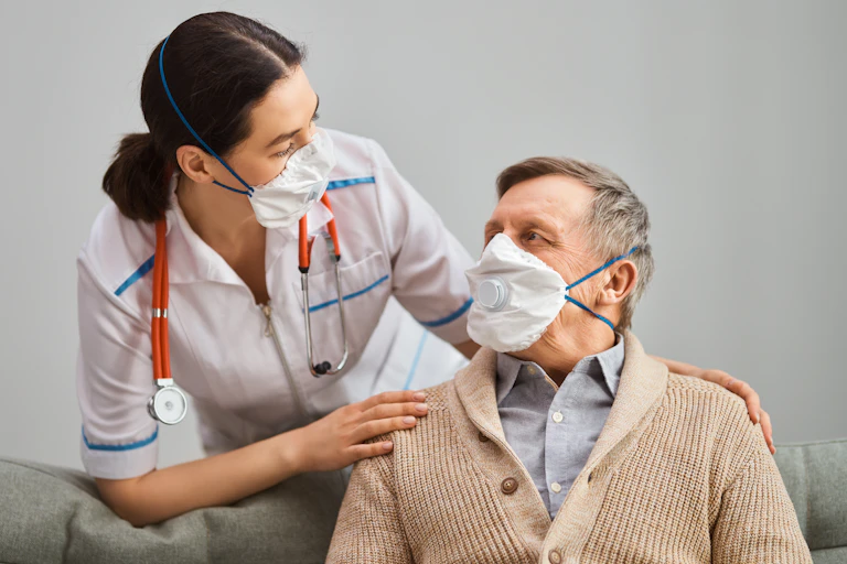 An older man, wearing a mask, interacting with a nurse