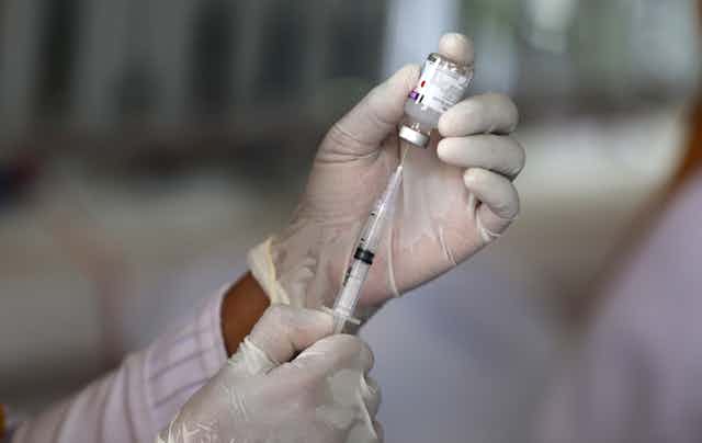 Gloved hands holding a vaccine phial and syringe