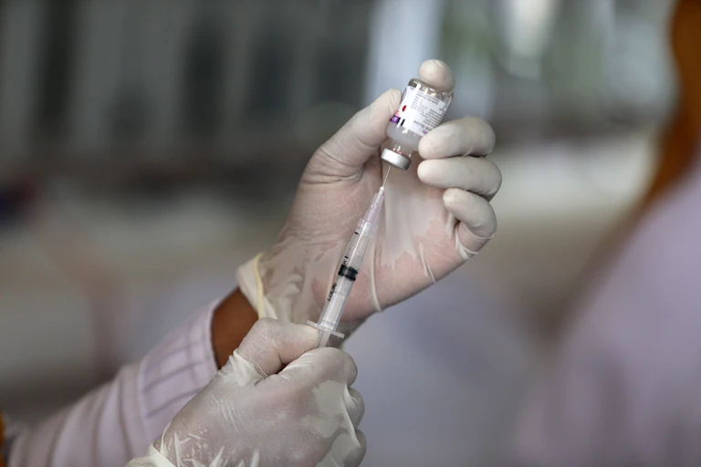Gloved hands holding a vaccine phial and syringe