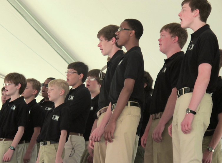 Ten boys ranging in age from roughly eight to 16, stand facing the same direction singing.