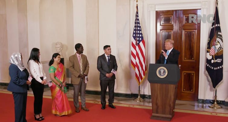 Trump stands with five new US citizens, with American flag in the background