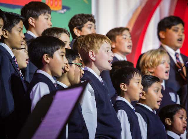 A medium shot of a boys choir, mid song. The boys are wearing vests and ties.