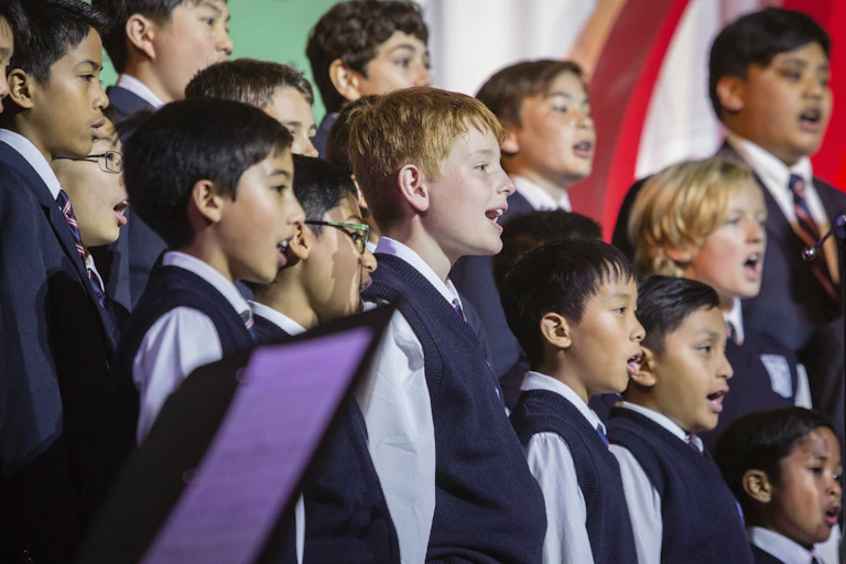 A medium shot of a boys choir, mid song. The boys are wearing vests and ties.