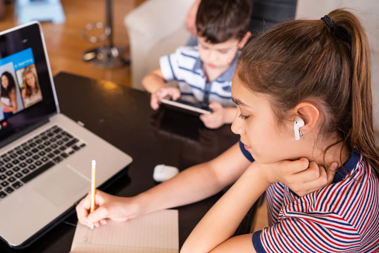 Teenager studying at home with a younger sibling nearby