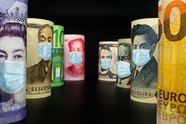 World currencies lining up with face masks on them