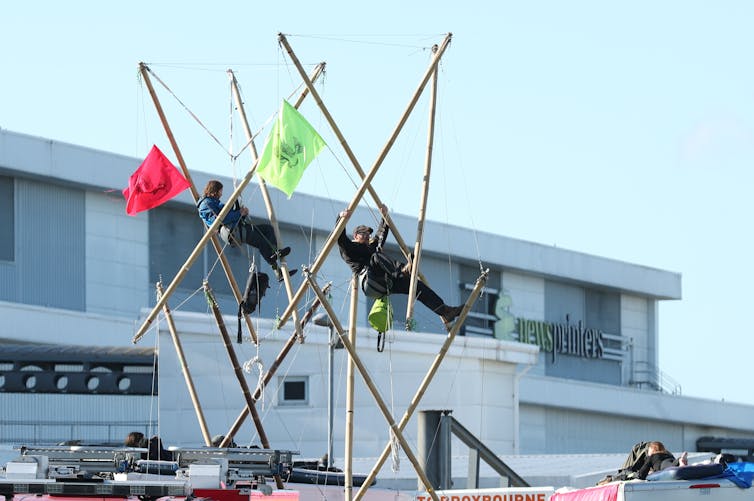 Two protesters are suspended in bamboo towers erected in front of a newspaper printing plant.