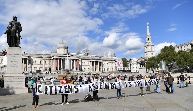 Activists stand in Trafalgar Square holding a banner reading 'Citizens' assembly is the answer'.