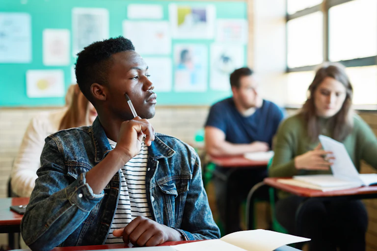 A young, black, male university student in an exam room with other students.