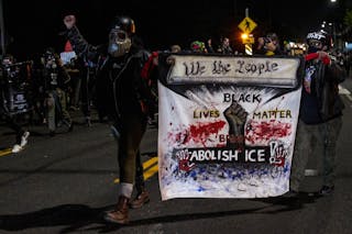 Protesters carry a banner reading 'Black Lives Matter,' 'Abolish ICE,' and 'We the People'
