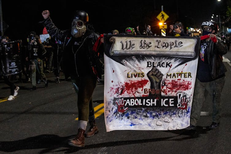 Protesters carry a banner reading 'Black Lives Matter,' 'Abolish ICE,' and 'We the People'