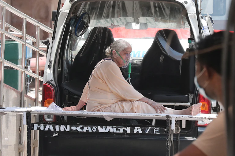 Woman sitting on stretcher with oxygen mask on in front of van.