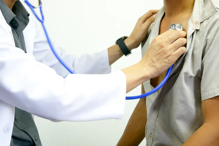 A person in a lab coat checking another person with a stethoscope.