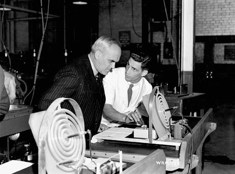 Two men lean over some scientific equipment.