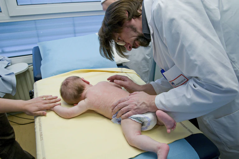 Baby with a rash, lying facedown while mom holds their hand in a doctor's office
