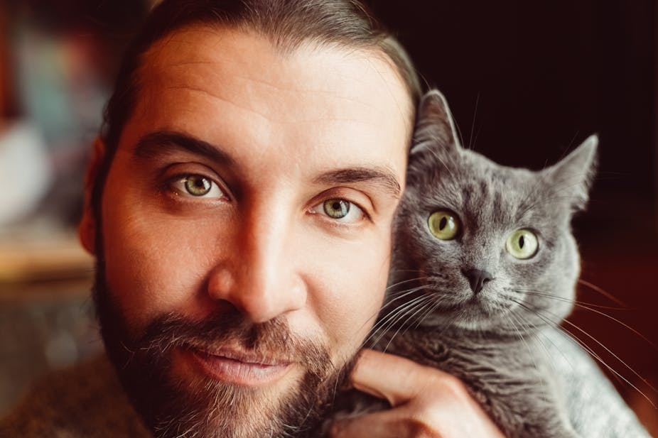 A bearded man poses with a gray cat.
