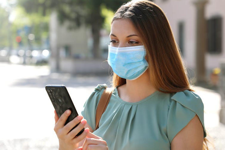 A woman wearing a face mask looks at her mobile phone.