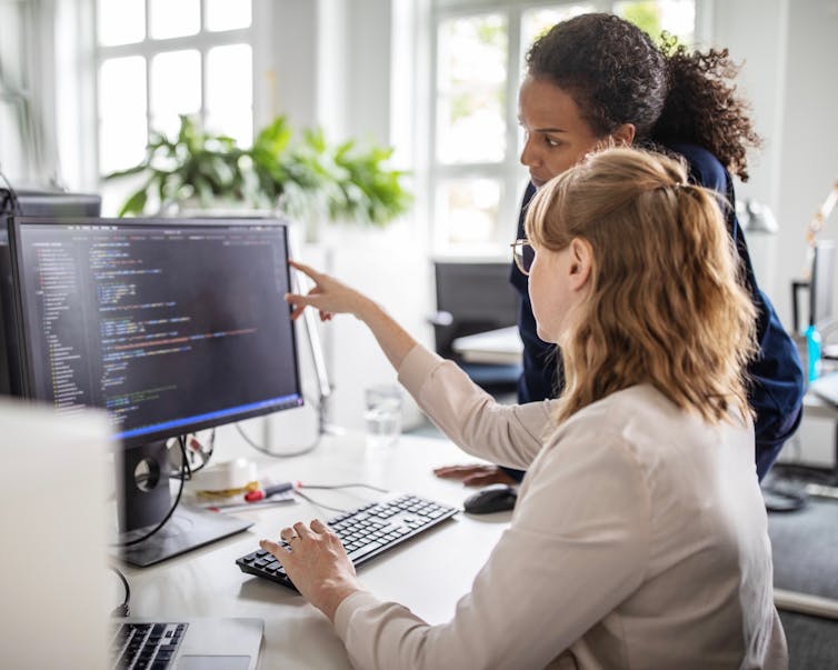 Two professional women discussing code on a computer screen.