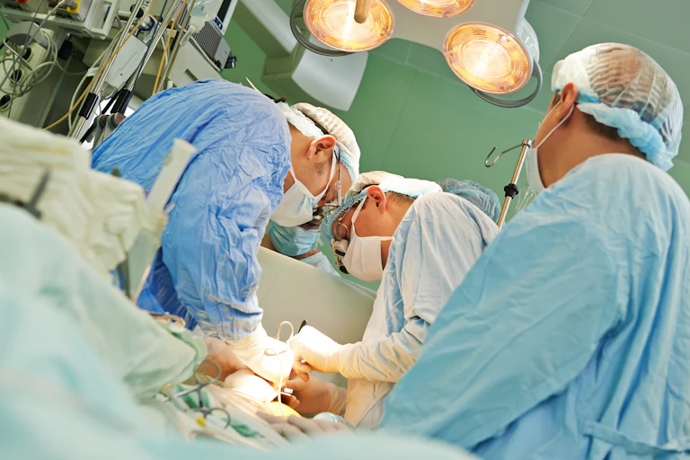 Three surgeons in blue scrubs work on a patient.
