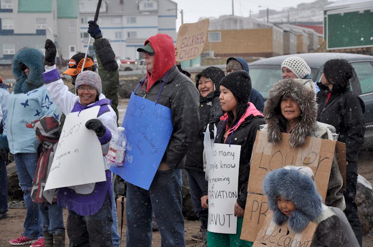 People wearing coats and hats hold up protest signs