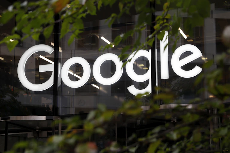 The Google logo in the window of an office building, partially obscured by trees.