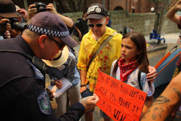 A policeman threatening to arrest a child who is protesting.