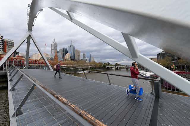 Two people walking across a footbridge in Melbourne. 