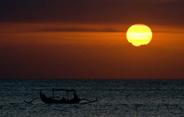 A traditional boat in the sea at a hot sunset in Bali.