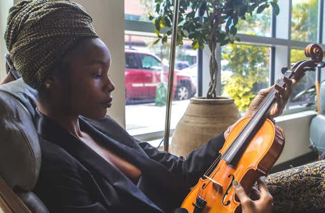 A Black woman wearing a headwrap gazes at a violin.
