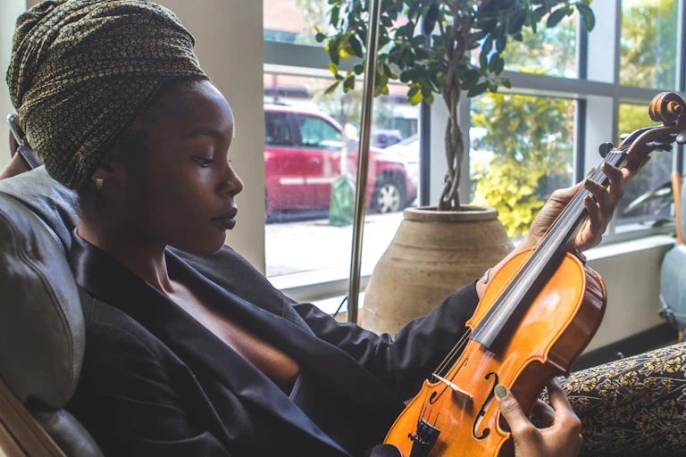 A Black woman wearing a headwrap gazes at a violin.