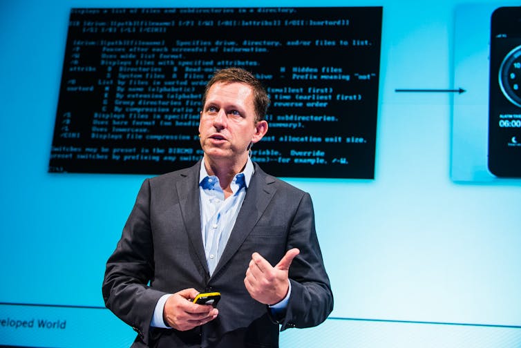 Peter Tiel stood in front of screen displaying computer code.