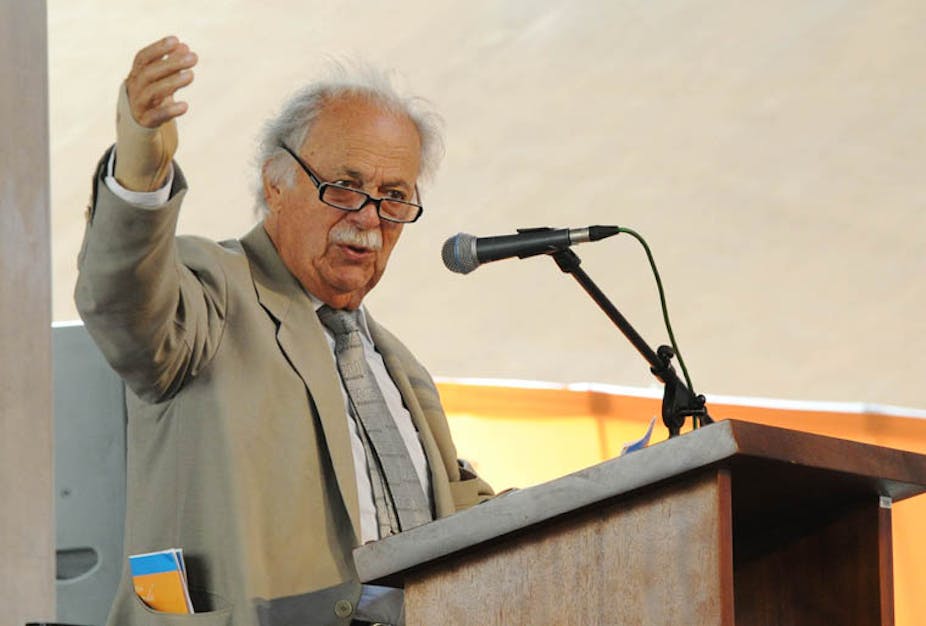 A white haired, balding and bespectacled George Bizos raises his right hand to emphasise a point during a speech