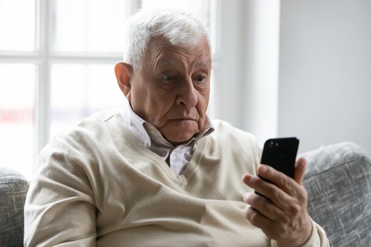 Old man sat on sofa looking confused at smartphone