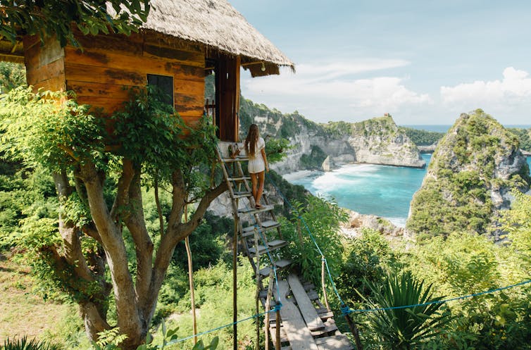Woman in tree house looking out at sea.