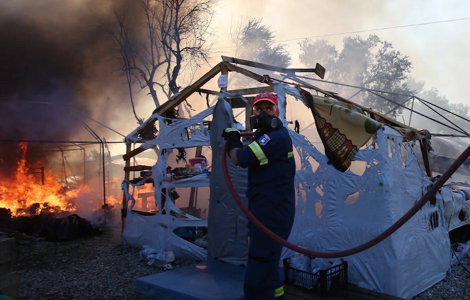 Fireman with hose in front of half burnt tent and fire.