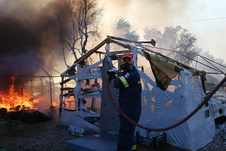 Fireman with hose in front of half burnt tent and fire.