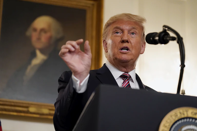 Trump gestures with his right hand while speaking behind a podium with a portrait of George Washington behind him.