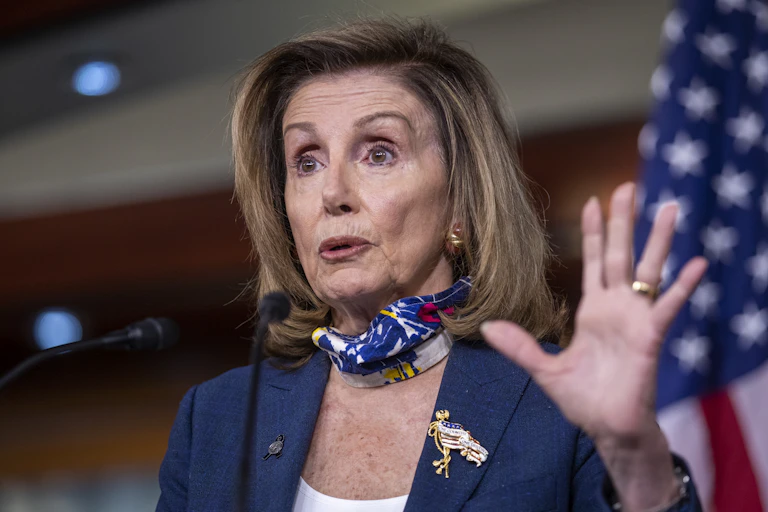Nancy Pelosi speaks into microphones and holds up hand